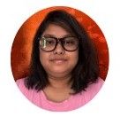 A woman with medium-length dark hair wearing large black-framed glasses and a pink T-shirt, standing against a textured orange-red background. She is looking straight at the camera with a neutral expression.