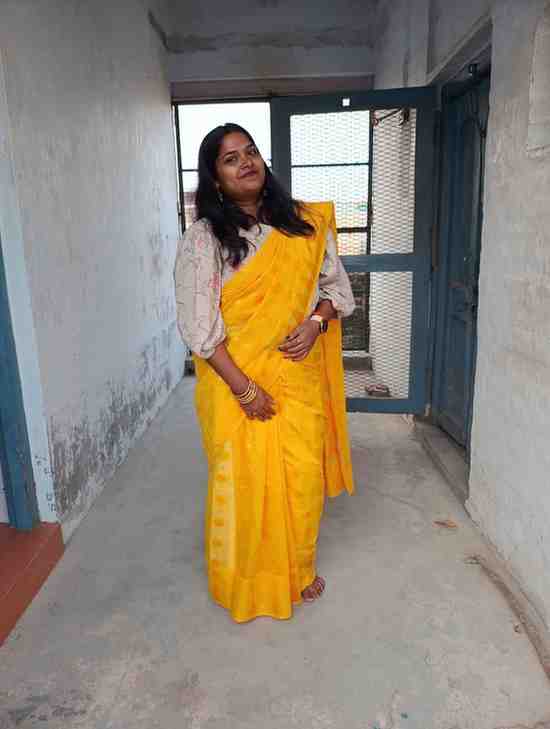 Woman wearing a vibrant yellow saree with a printed blouse, standing in a sunlit corridor with a confident smile.